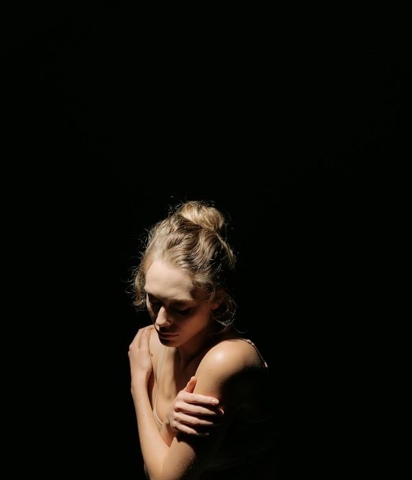 Woman in a calm yoga pose on a dark, velvet-like background with soft lighting.